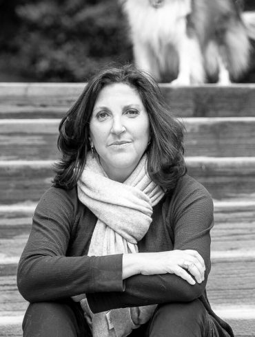 Image of Author Laura Zigman sitting on steps with a blurry dog in the background